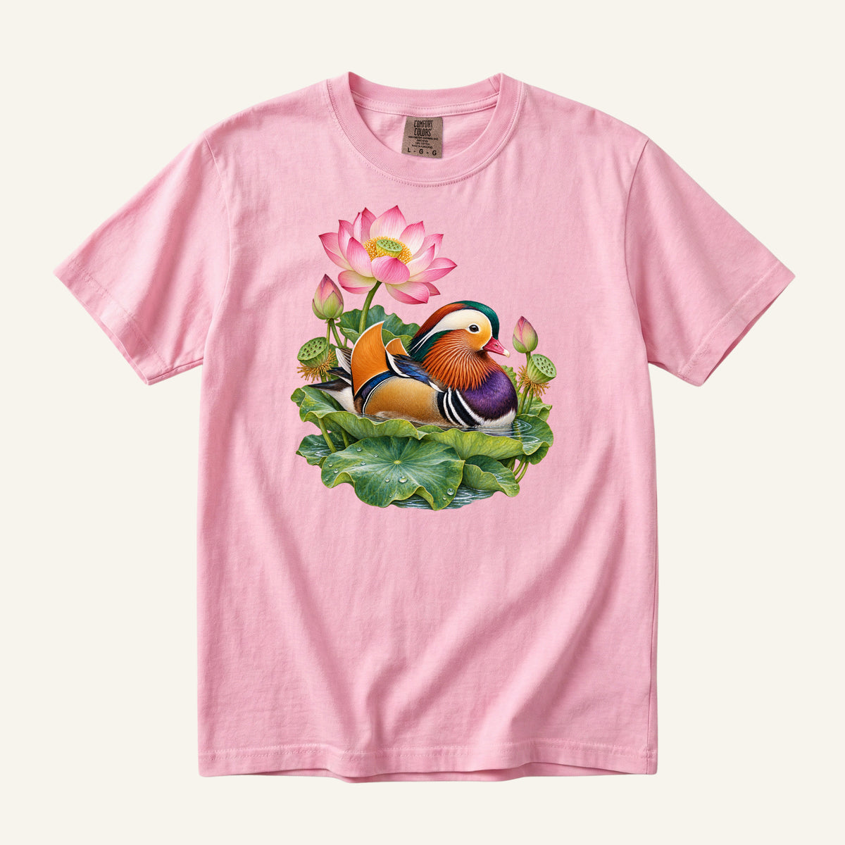 Mandarin duck with orange sail feathers and a purple breast among pink lotus blossoms and green leaves, printed on a Blossom pink Comfort Colors 1717 unisex t-shirt
