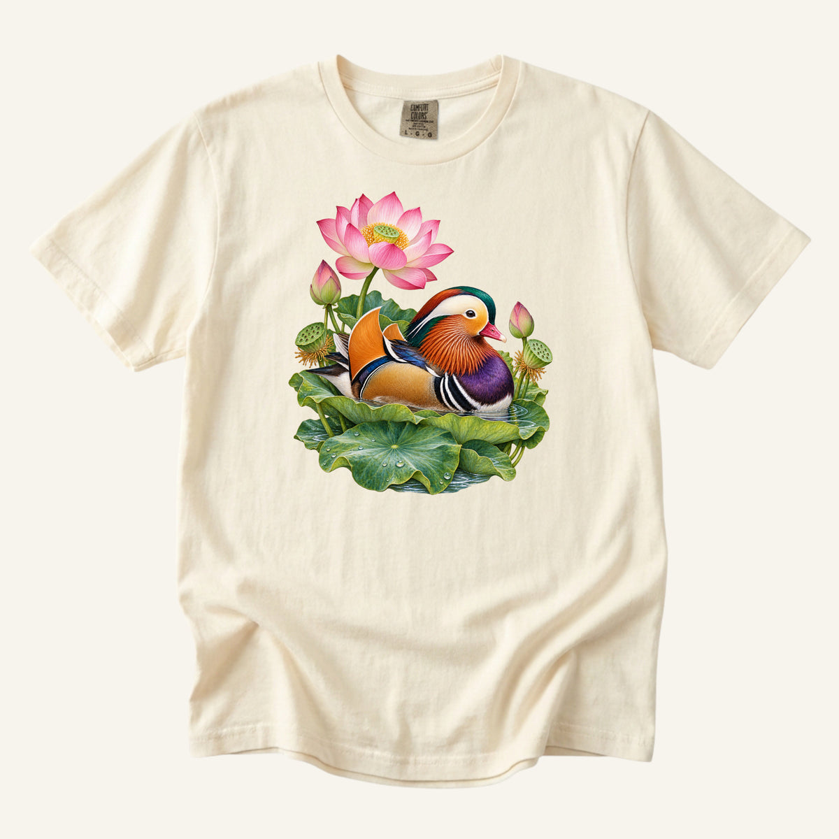 Mandarin duck with orange sail feathers and a purple breast among pink lotus blossoms and green leaves, printed on an Ivory Comfort Colors 1717 unisex t-shirt