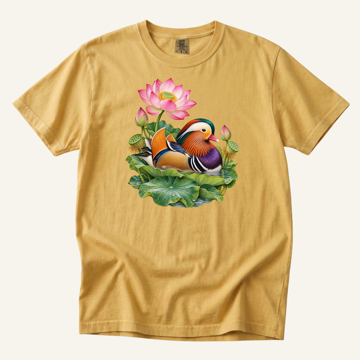 Mandarin duck with orange sail feathers and a purple breast among pink lotus blossoms and green leaves, printed on a Mustard yellow Comfort Colors 1717 unisex t-shirt