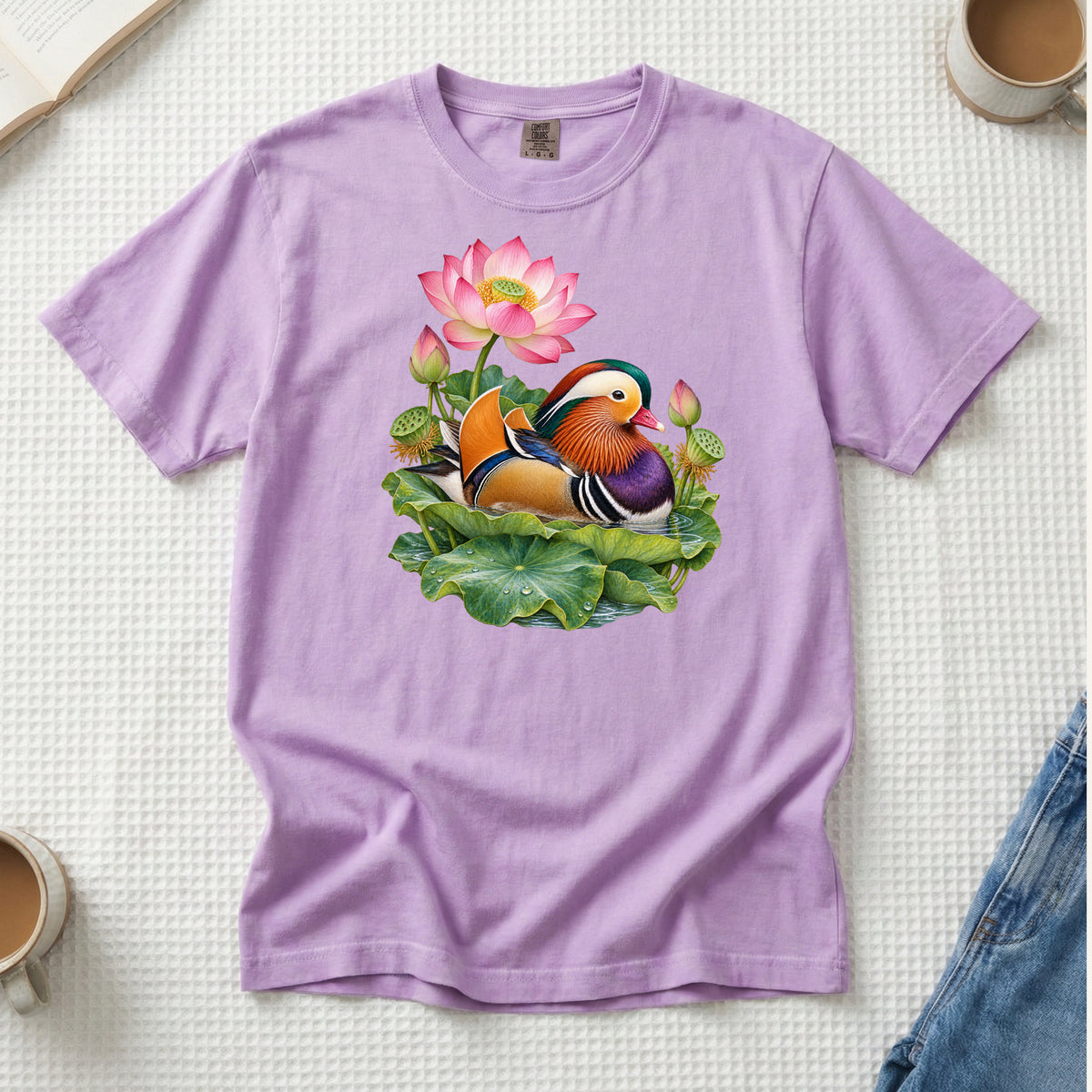 Mandarin duck with orange sail feathers and a purple breast among pink lotus blossoms and green leaves, printed on an Orchid lavender Comfort Colors 1717 unisex t-shirt