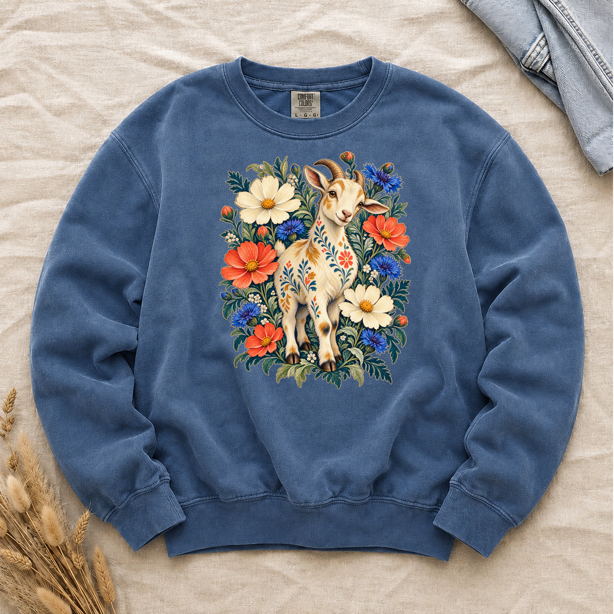 Folk-art goat patterned with flowers among coral and blue blooms on a Blue Jean denim Comfort Colors crewneck sweatshirt