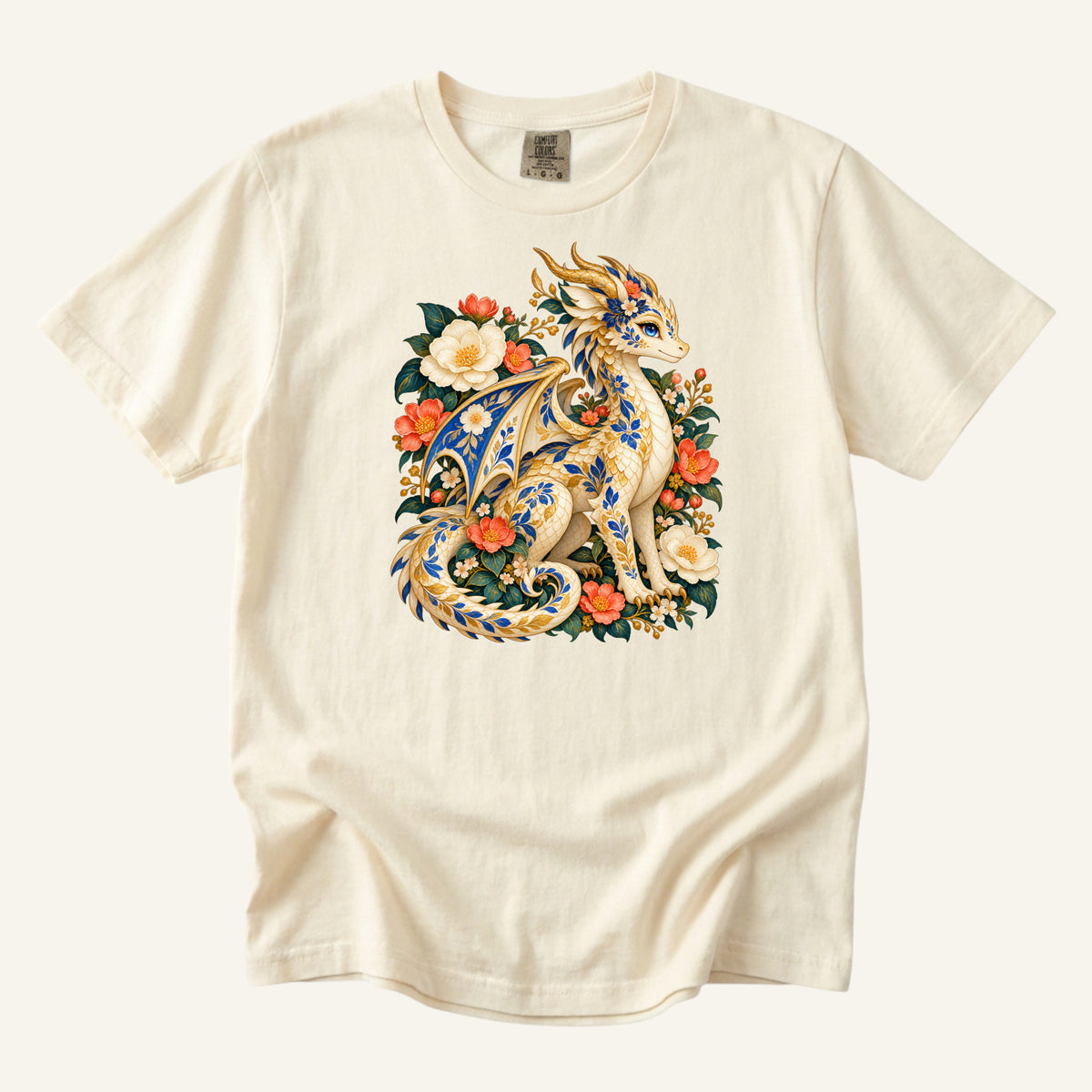The Garden Was Her Gold floral dragon t-shirt in Ivory, a cream-and-gold dragon patterned with blue botanical ornament like painted porcelain, seated among coral-red flowers, ivory blossoms and deep green foliage
