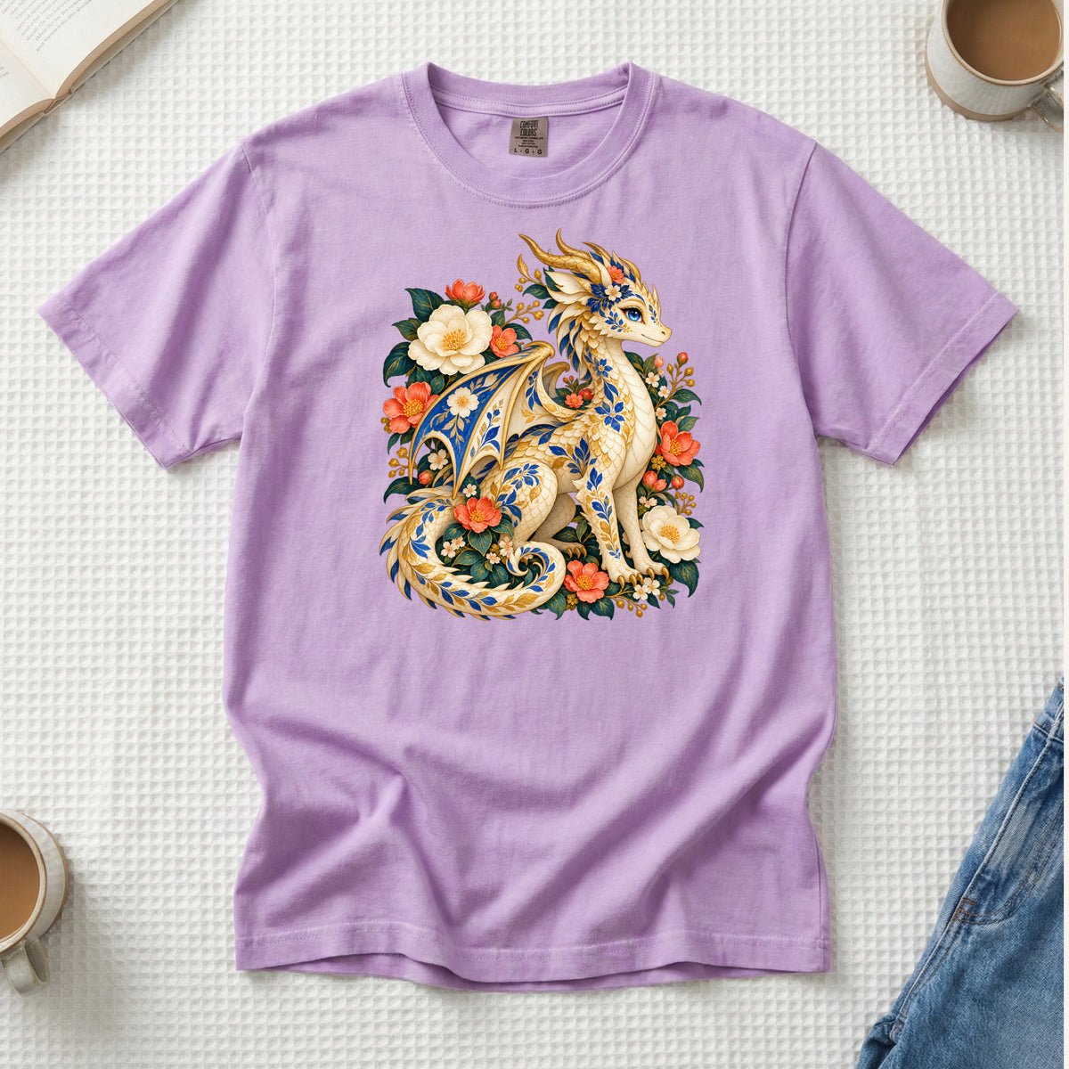 The Garden Was Her Gold floral dragon t-shirt in Orchid, a cream-and-gold dragon patterned with blue botanical ornament like painted porcelain, seated among coral-red flowers, ivory blossoms and deep green foliage