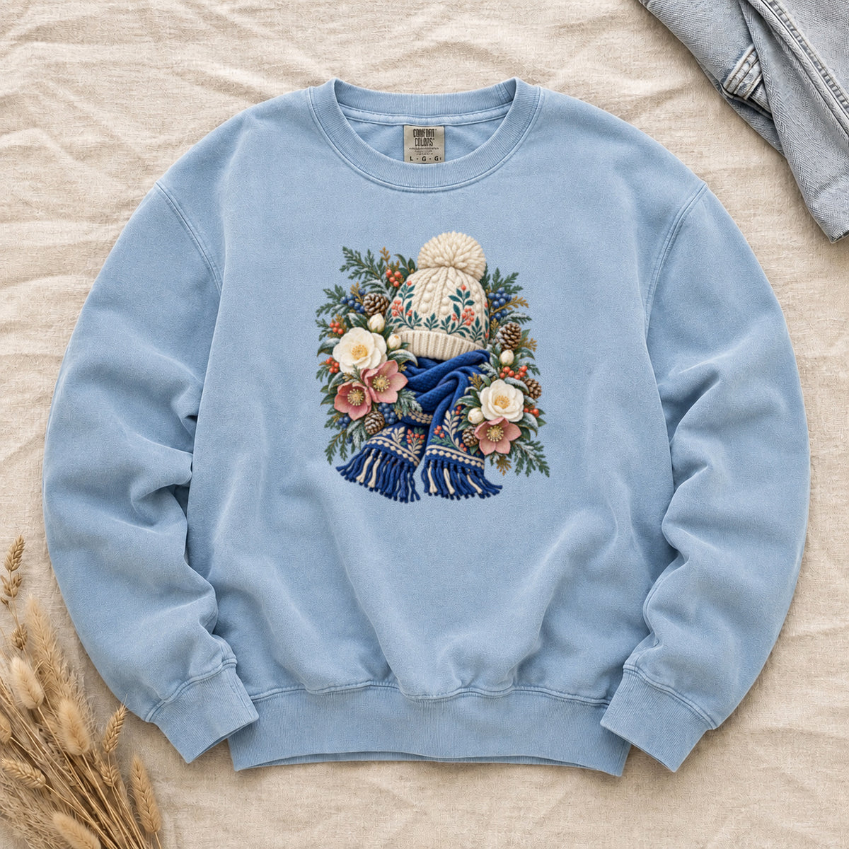 Floral Knit Hat & Scarf Sweatshirt in Chambray — a cream pom-pom hat patterned in teal and coral above a deep blue fringed scarf, framed by evergreen, pinecones, red berries and cream roses