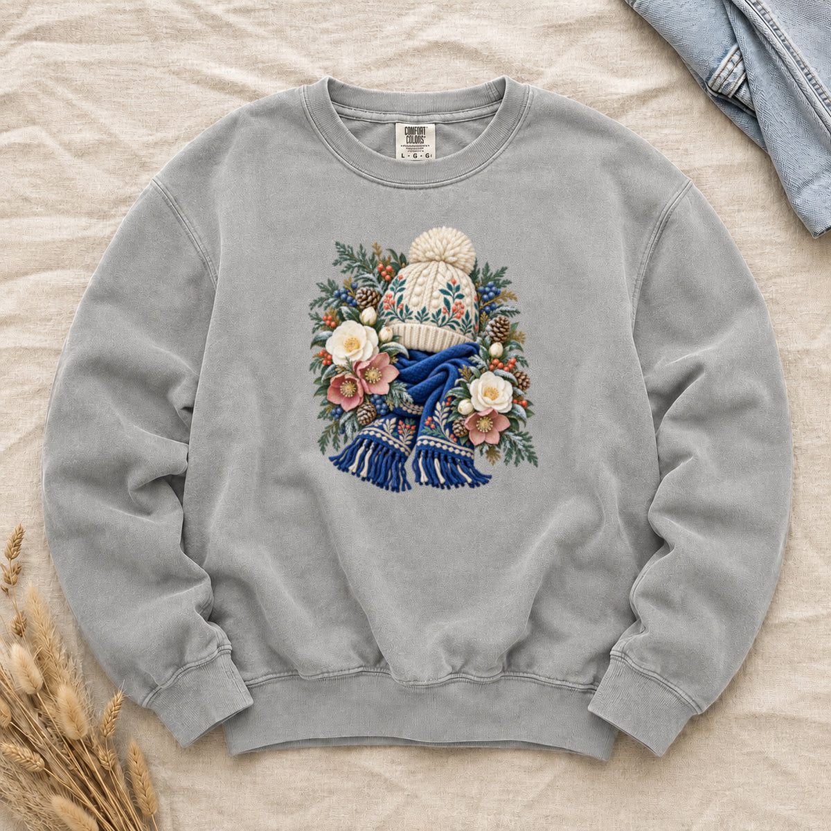 Floral Knit Hat & Scarf Sweatshirt in Grey — a cream pom-pom hat patterned in teal and coral above a deep blue fringed scarf, framed by evergreen, pinecones, red berries and cream roses