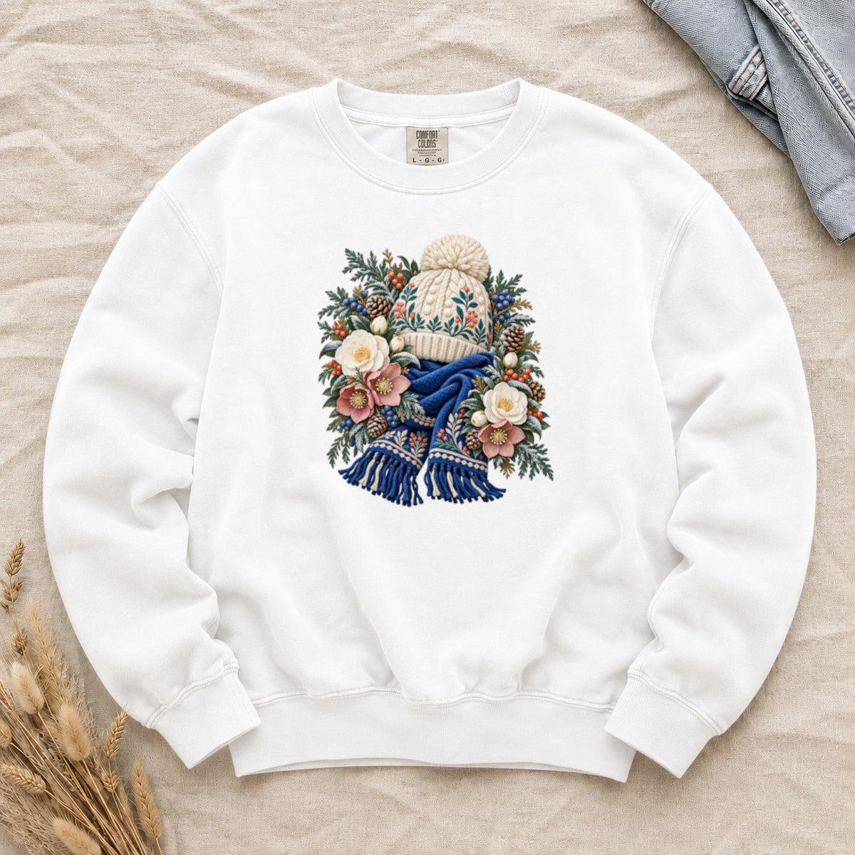 Floral Knit Hat & Scarf Sweatshirt in White — a cream pom-pom hat patterned in teal and coral above a deep blue fringed scarf, framed by evergreen, pinecones, red berries and cream roses