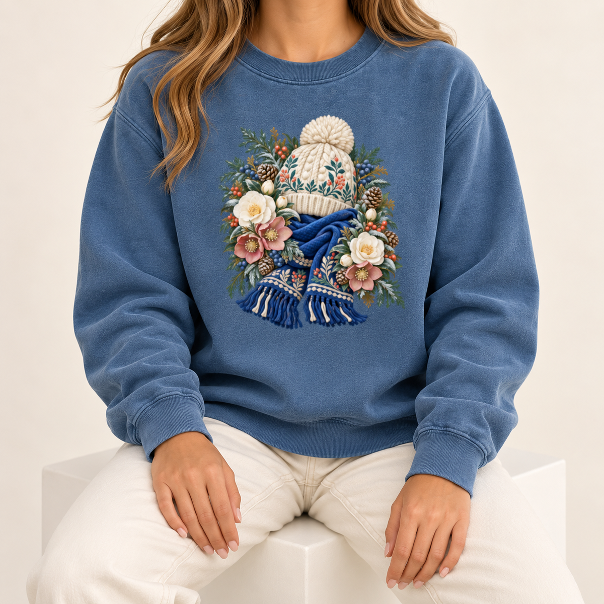 Floral knit hat and scarf design on a heavyweight garment-dyed Comfort Colors 1566 crewneck — a cream pom-pom hat above a deep blue fringed scarf, framed by evergreen, pinecones and cream roses