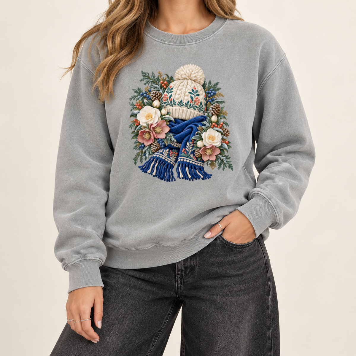 Floral knit hat and scarf print on a 9.5 oz garment-dyed cotton-blend crewneck — a cream pom-pom hat above a deep blue fringed scarf, framed by evergreen, pinecones and cream roses