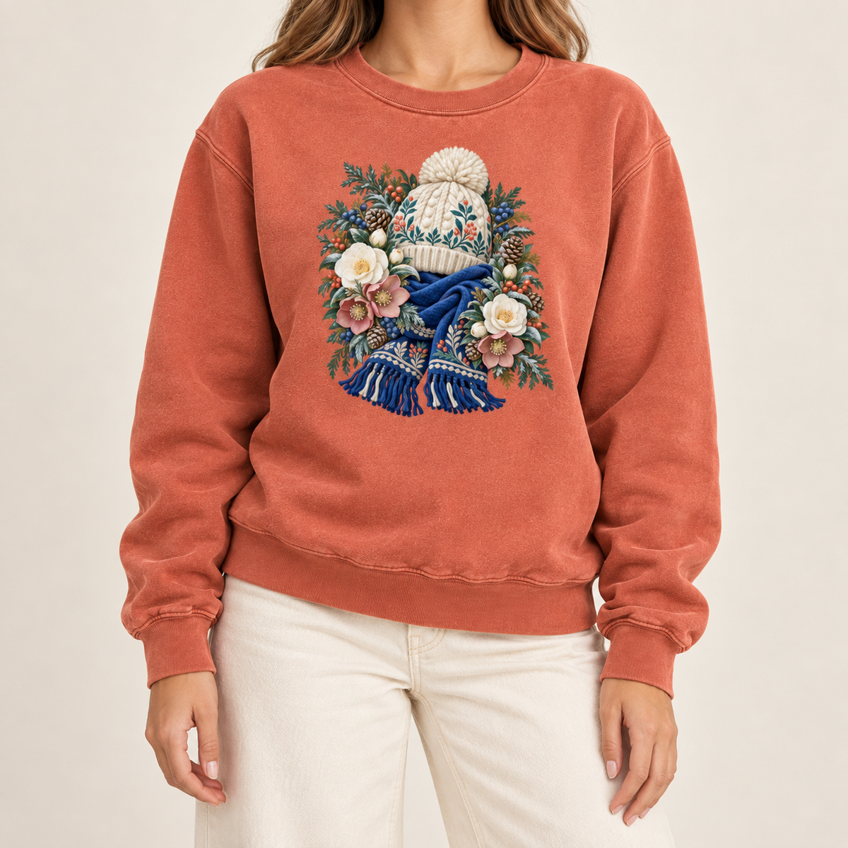 Winter walk hat and scarf sweatshirt, large front-centered print, no lettering — a cream pom-pom hat above a deep blue fringed scarf, framed by evergreen, pinecones and cream roses
