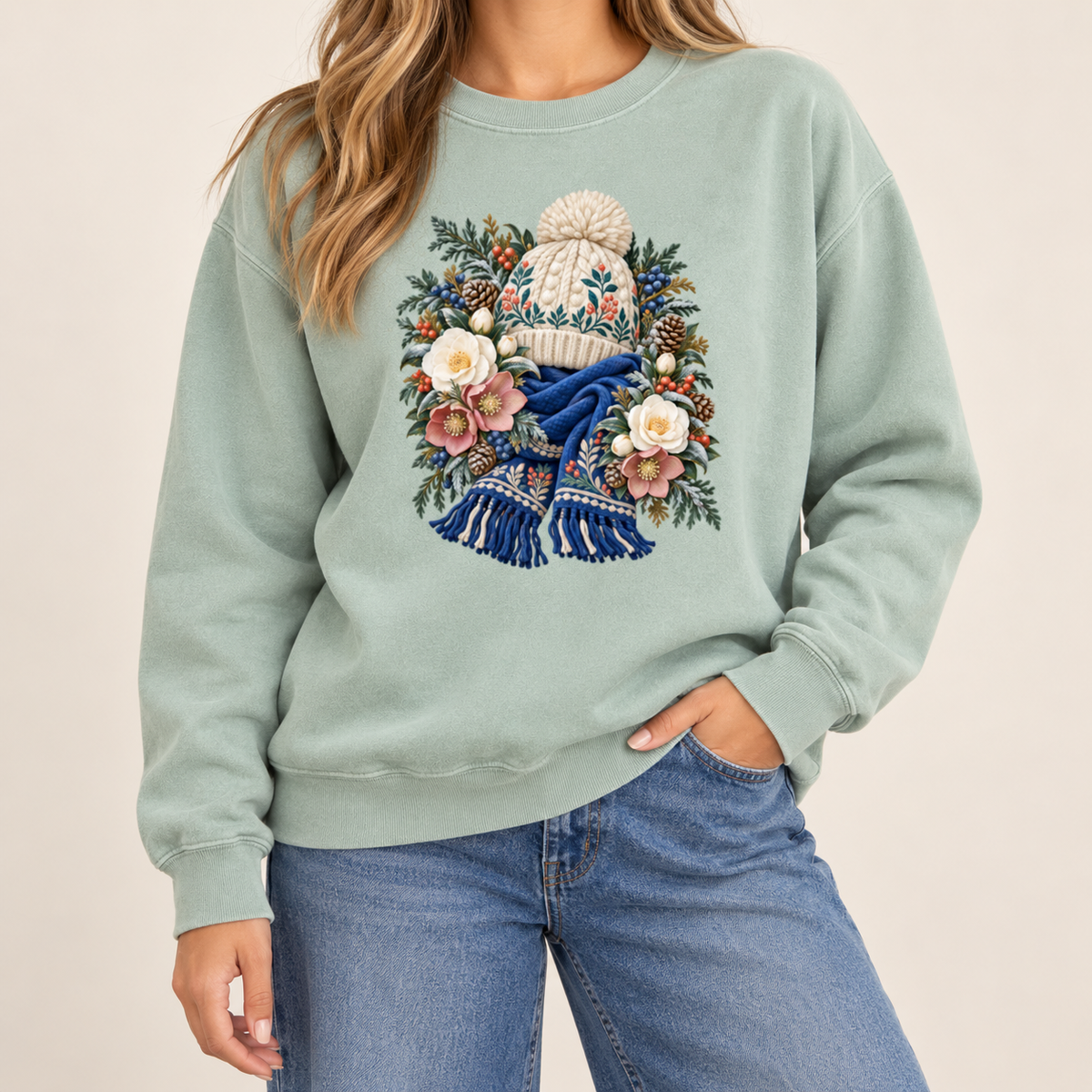 Vintage winter botanical hat and scarf design on a side-seamed Comfort Colors 1566 crewneck — a cream pom-pom hat above a deep blue fringed scarf, framed by evergreen, pinecones and cream roses