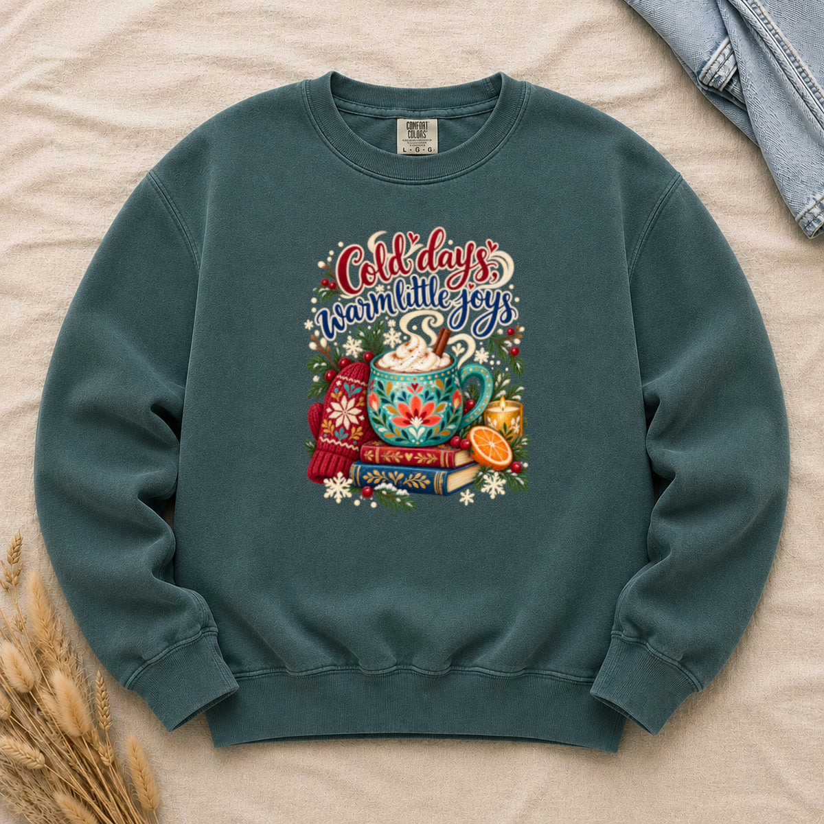 Cocoa and books winter sweatshirt in Blue Spruce, a deep green garment-dyed Comfort Colors crewneck printed with a mug of cocoa and marshmallows on a stack of books, with mittens, orange slices, cinnamon and evergreen around it