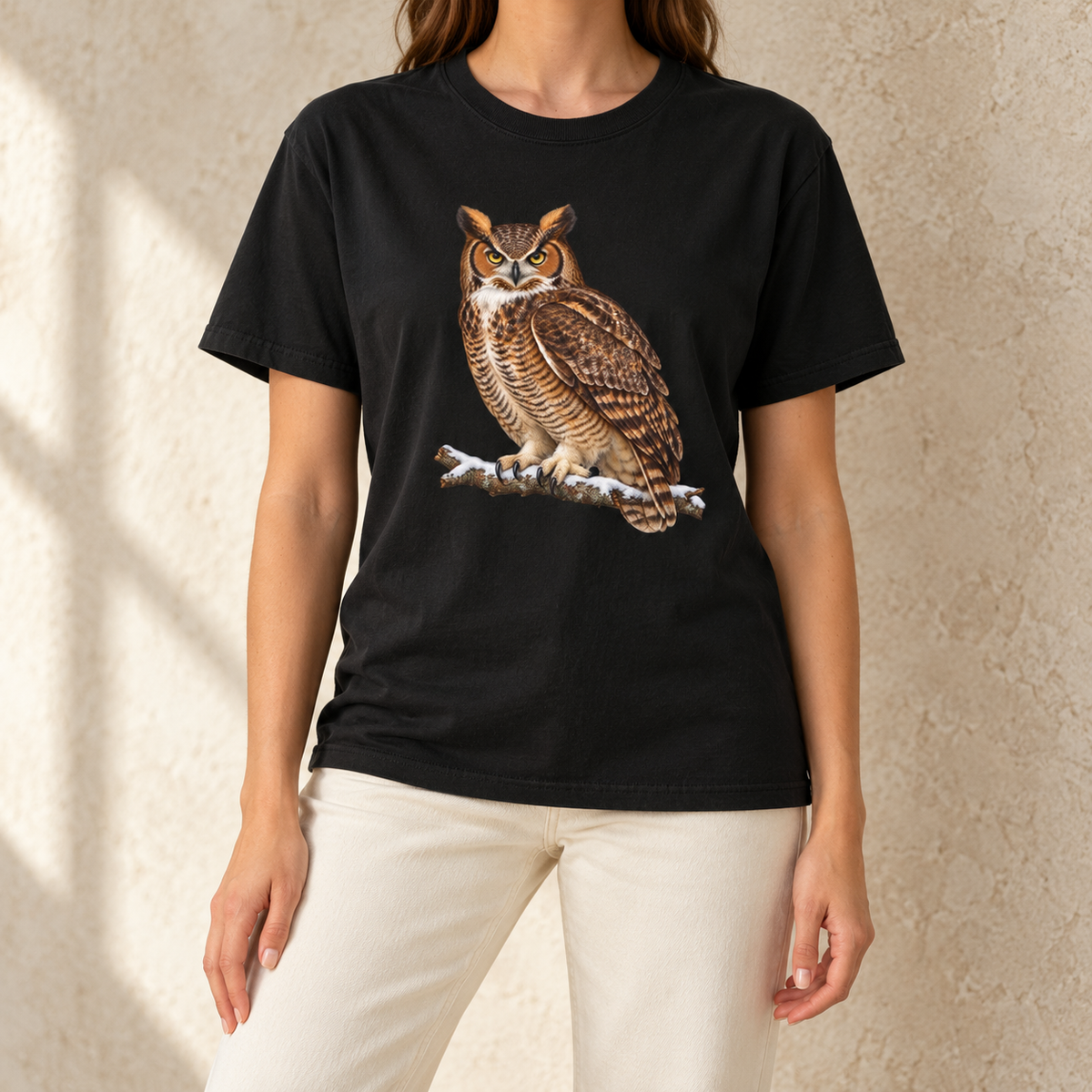 Great horned owl t-shirt worn by a woman – a watercolor great horned owl with ear tufts and yellow eyes on a snowy branch, printed large on a garment-dyed Comfort Colors cotton tee