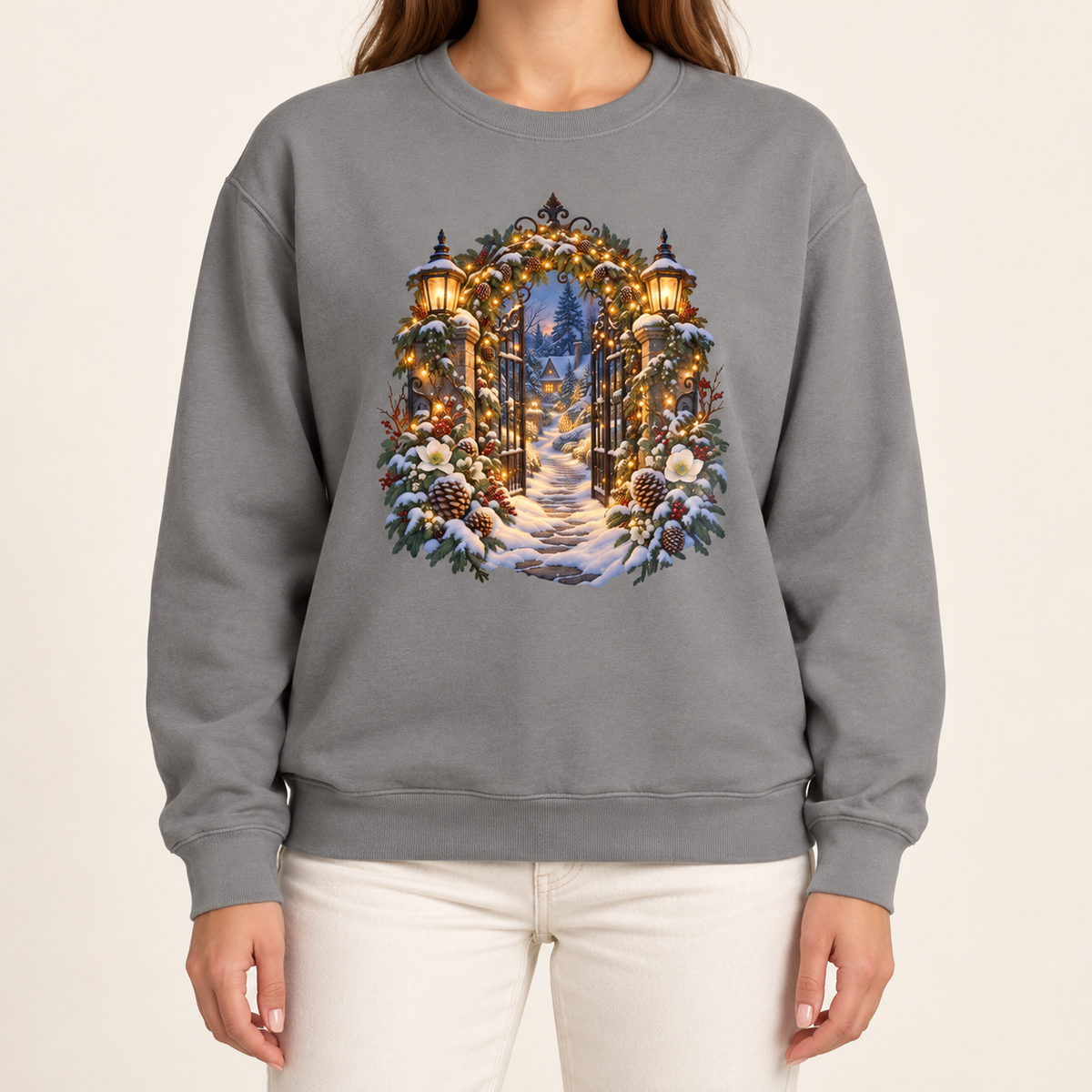 Christmas garden gate sweatshirt in Grey: an open iron gate with lantern-topped pillars and a snowy path to a lit cottage, on a soft heather gray garment-dyed Comfort Colors crewneck