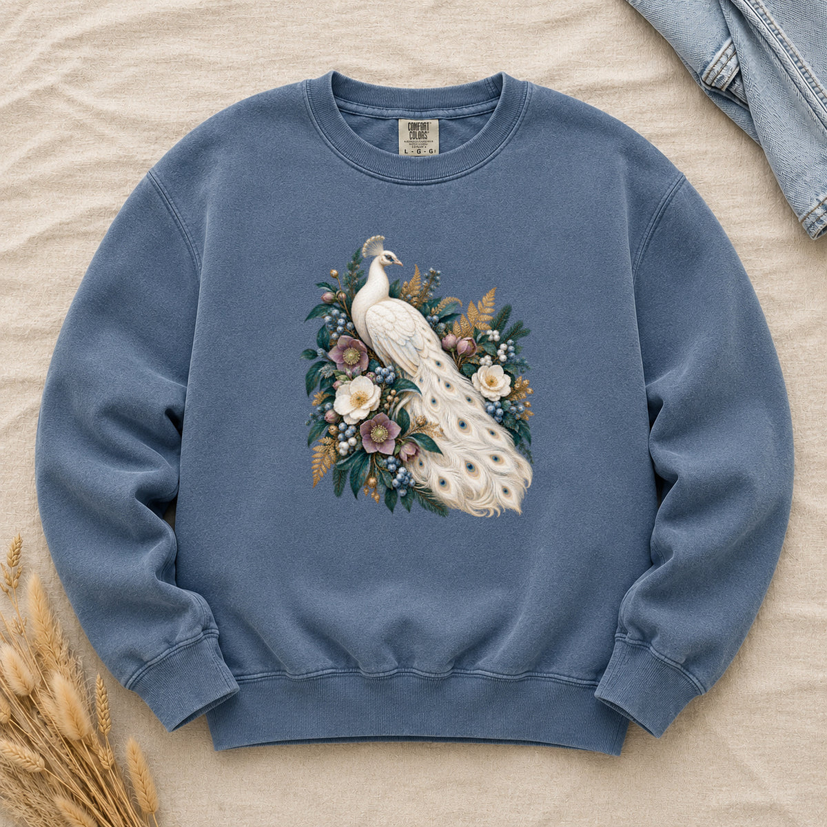 Ivory Peacock and Floral Sweatshirt in Denim — an ivory peacock among cream and dusty purple flowers, blue berries and deep green leaves, its long tail curving down through the arrangement with small blue and gold markings on the pale feathers