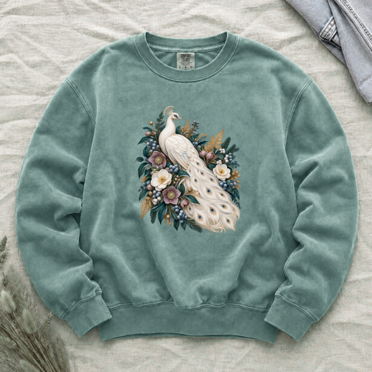 Ivory Peacock and Floral Sweatshirt in Light Green — an ivory peacock among cream and dusty purple flowers, blue berries and deep green leaves, its long tail curving down through the arrangement with small blue and gold markings on the pale feathers