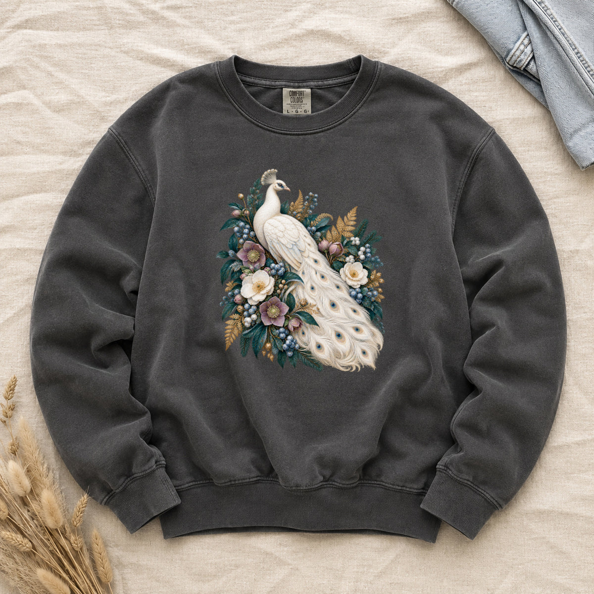 Ivory Peacock and Floral Sweatshirt in Pepper — an ivory peacock among cream and dusty purple flowers, blue berries and deep green leaves, its long tail curving down through the arrangement with small blue and gold markings on the pale feathers