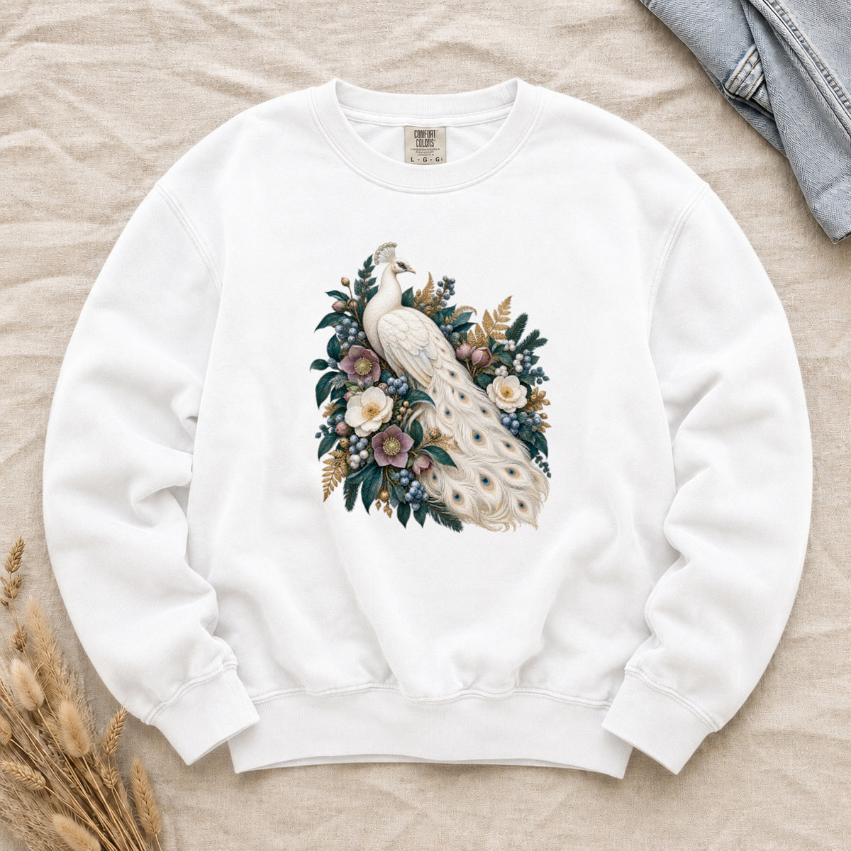 Ivory Peacock and Floral Sweatshirt in White — an ivory peacock among cream and dusty purple flowers, blue berries and deep green leaves, its long tail curving down through the arrangement with small blue and gold markings on the pale feathers