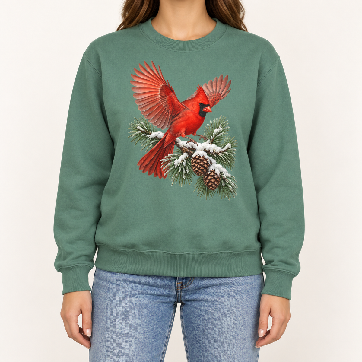 Cardinal in flight sweatshirt in Light Green – a male northern cardinal with wings spread landing on a snow-covered pine bough with pinecones, printed large on the chest of a Comfort Colors crewneck