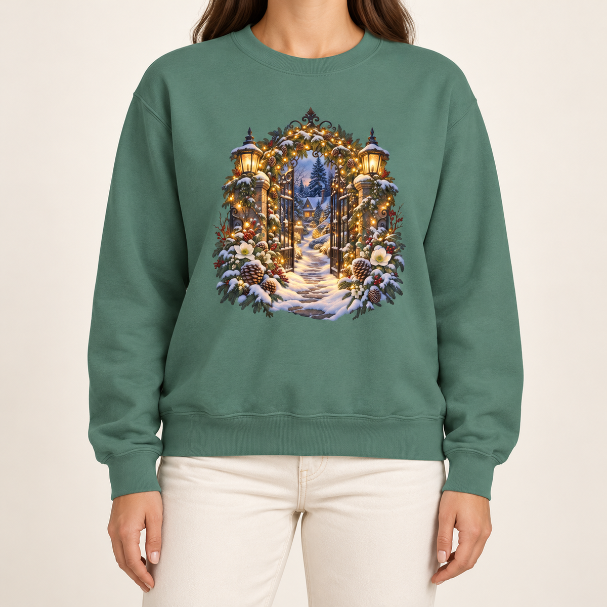 Christmas garden gate sweatshirt in Light Green: an open iron gate with lantern-topped pillars and a snowy path to a lit cottage, on a soft sage garment-dyed Comfort Colors crewneck