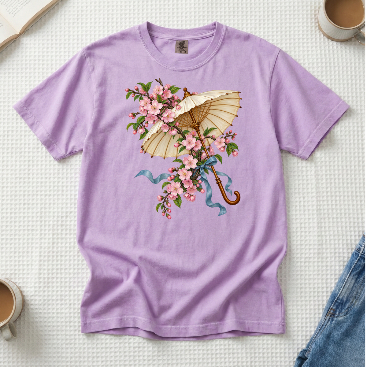 Meet Me Under the Blossoms tee in Orchid, a cream parasol with a blue ribbon among pink flowering branches