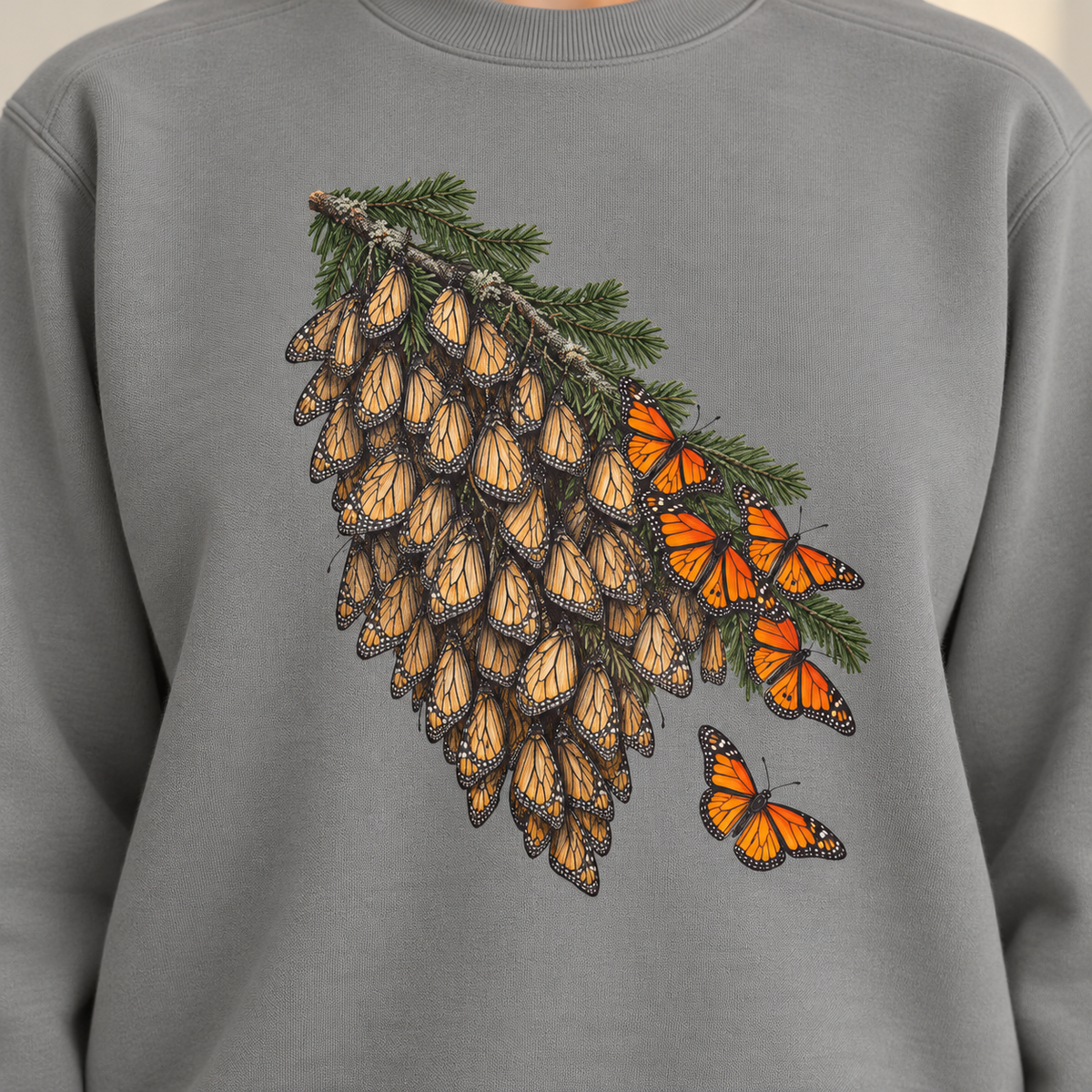 Close-up of the overwintering monarchs print on a Grey Comfort Colors crewneck - closed tan wings packed along a fir bough, open orange wings at the edge