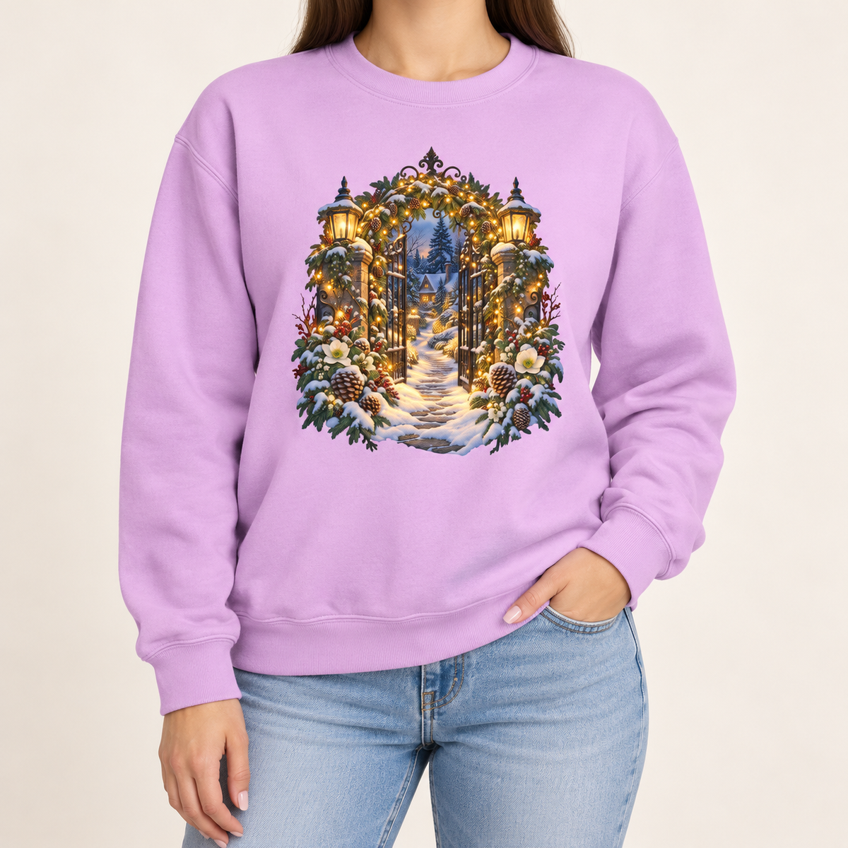 Christmas garden gate sweatshirt in Orchid: an open iron gate with lantern-topped pillars and a snowy path to a lit cottage, on a light lavender garment-dyed Comfort Colors crewneck