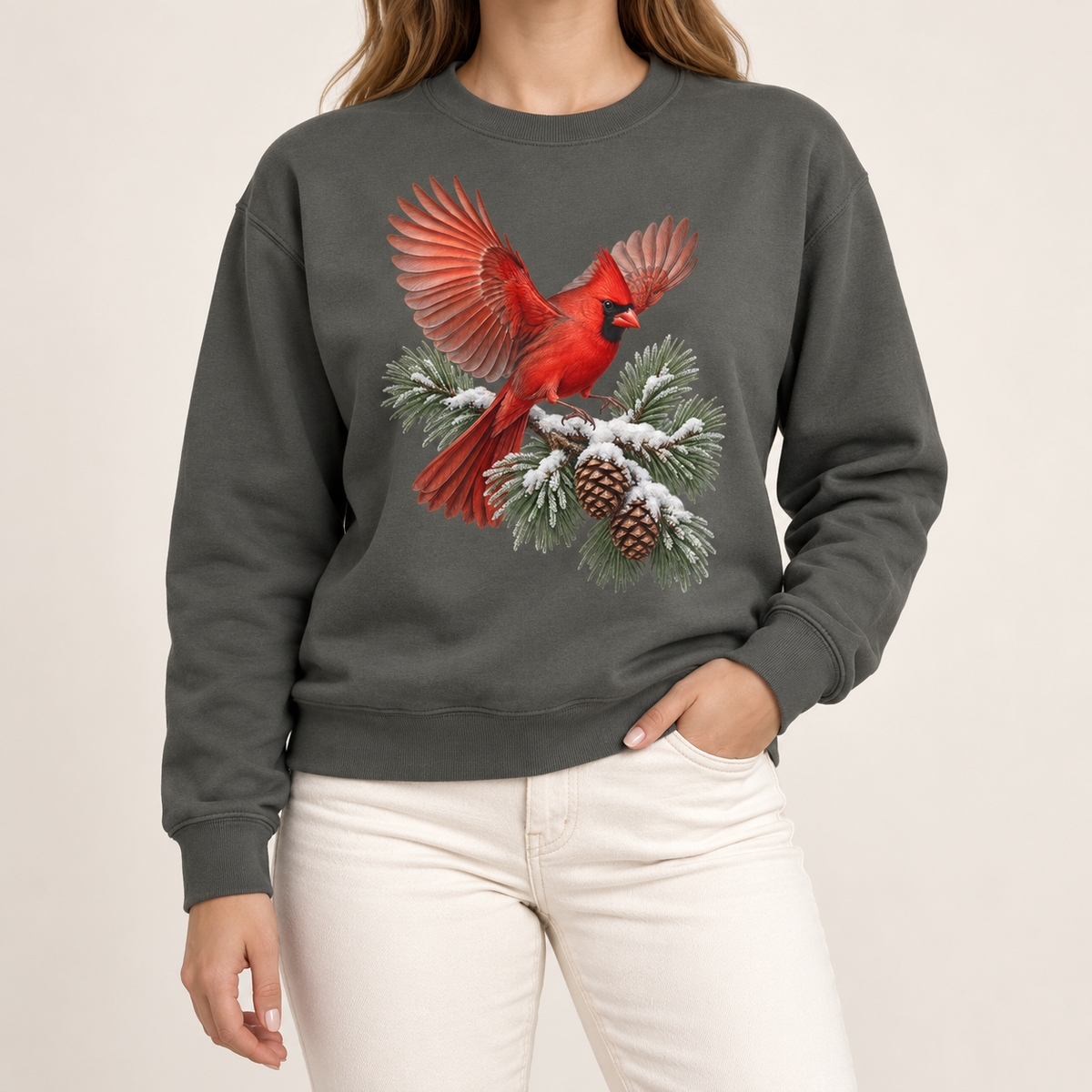Cardinal in flight sweatshirt in Pepper – a male northern cardinal with wings spread landing on a snow-covered pine bough with pinecones, printed large on the chest of a Comfort Colors crewneck