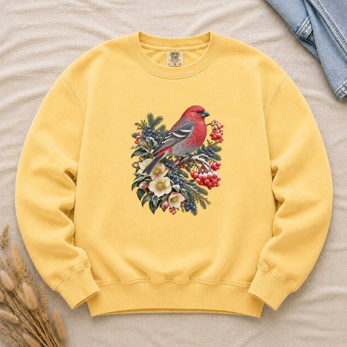 Red Bird & Winter Botanicals Sweatshirt in Butter — a bright red bird with softly shaded gray wings and a long tail, perched on a branch among evergreen sprigs, red and blue berries and cream flowers