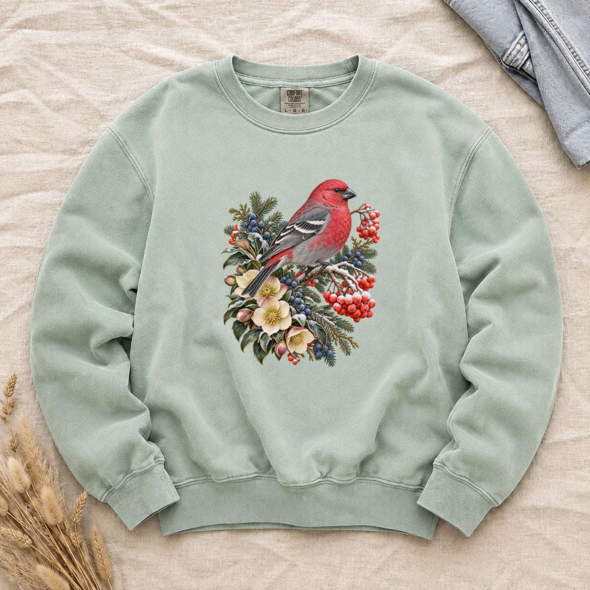 Red Bird & Winter Botanicals Sweatshirt in Chalky Mint — a bright red bird with softly shaded gray wings and a long tail, perched on a branch among evergreen sprigs, red and blue berries and cream flowers