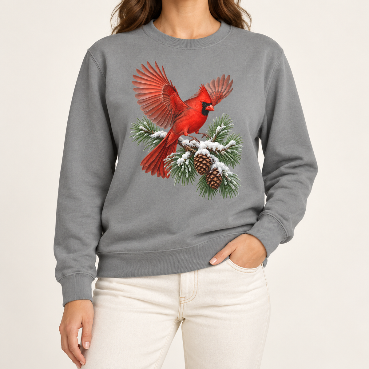 Cardinal in flight sweatshirt in Grey – a male northern cardinal with wings spread landing on a snow-covered pine bough with pinecones, printed large on the chest of a Comfort Colors crewneck