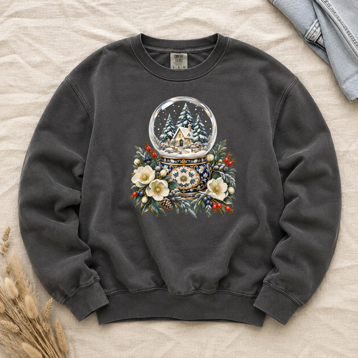 Snow Globe & Winter Florals Sweatshirt in Pepper — a glass snow globe holding a snowy cottage and evergreens on an ornate navy-and-gold base, framed by cream blossoms, pinecones and red berries