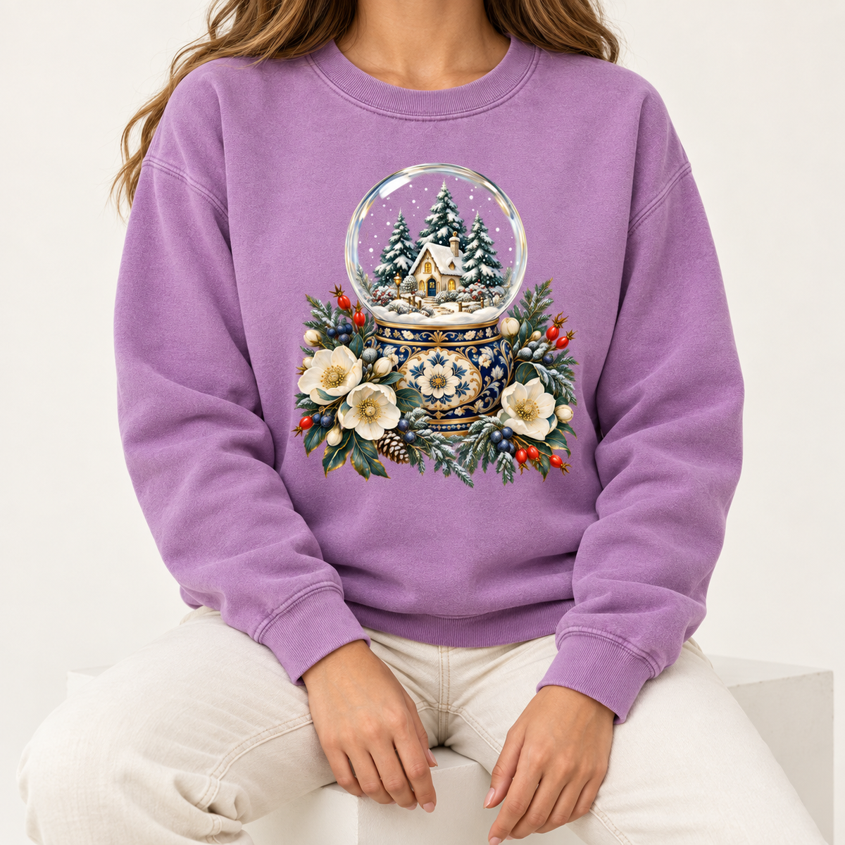 Snow globe and winter florals print on a 9.5 oz garment-dyed cotton-blend crewneck — a glass snow globe holding a snowy cottage and evergreens on an ornate navy-and-gold base, framed by cream blossoms and red berries