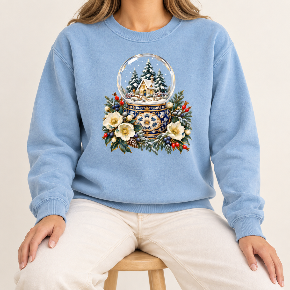 Snow globe and winter florals crewneck with 1x1 ribbed collar, cuffs and waistband — a glass snow globe holding a snowy cottage and evergreens on an ornate navy-and-gold base, framed by cream blossoms and red berries