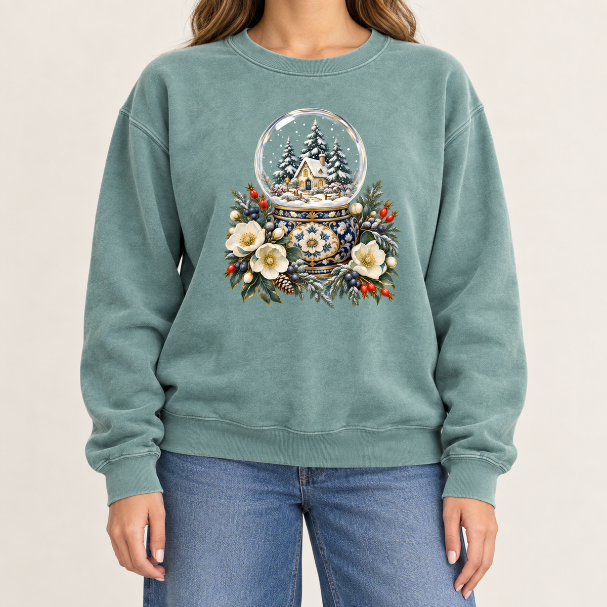 Winter cottage snow globe sweatshirt, large front-centered print, no lettering — a glass snow globe holding a snowy cottage and evergreens on an ornate navy-and-gold base, framed by cream blossoms and red berries