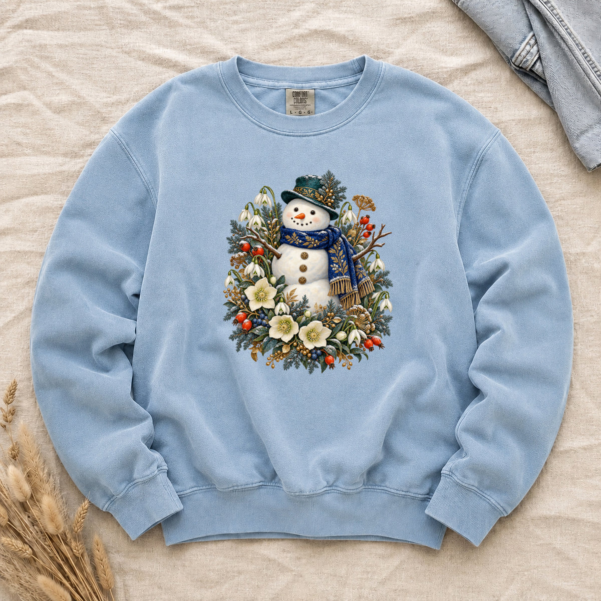 Snowman & Winter Botanicals Sweatshirt in Chambray — a smiling snowman in a decorated dark hat and a deep blue scarf with golden pattern, among evergreen branches, red berries and large cream flowers