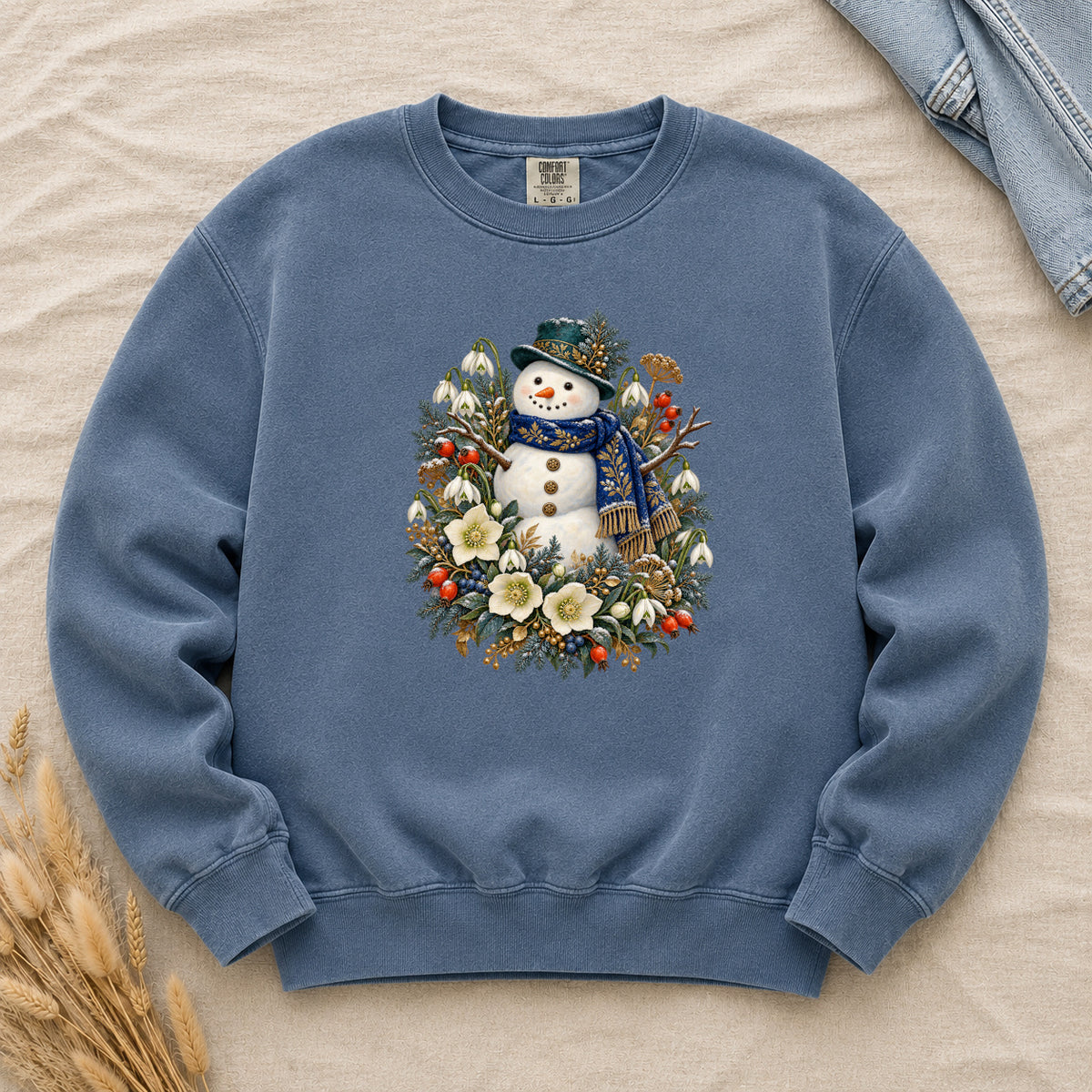 Snowman & Winter Botanicals Sweatshirt in Denim — a smiling snowman in a decorated dark hat and a deep blue scarf with golden pattern, among evergreen branches, red berries and large cream flowers