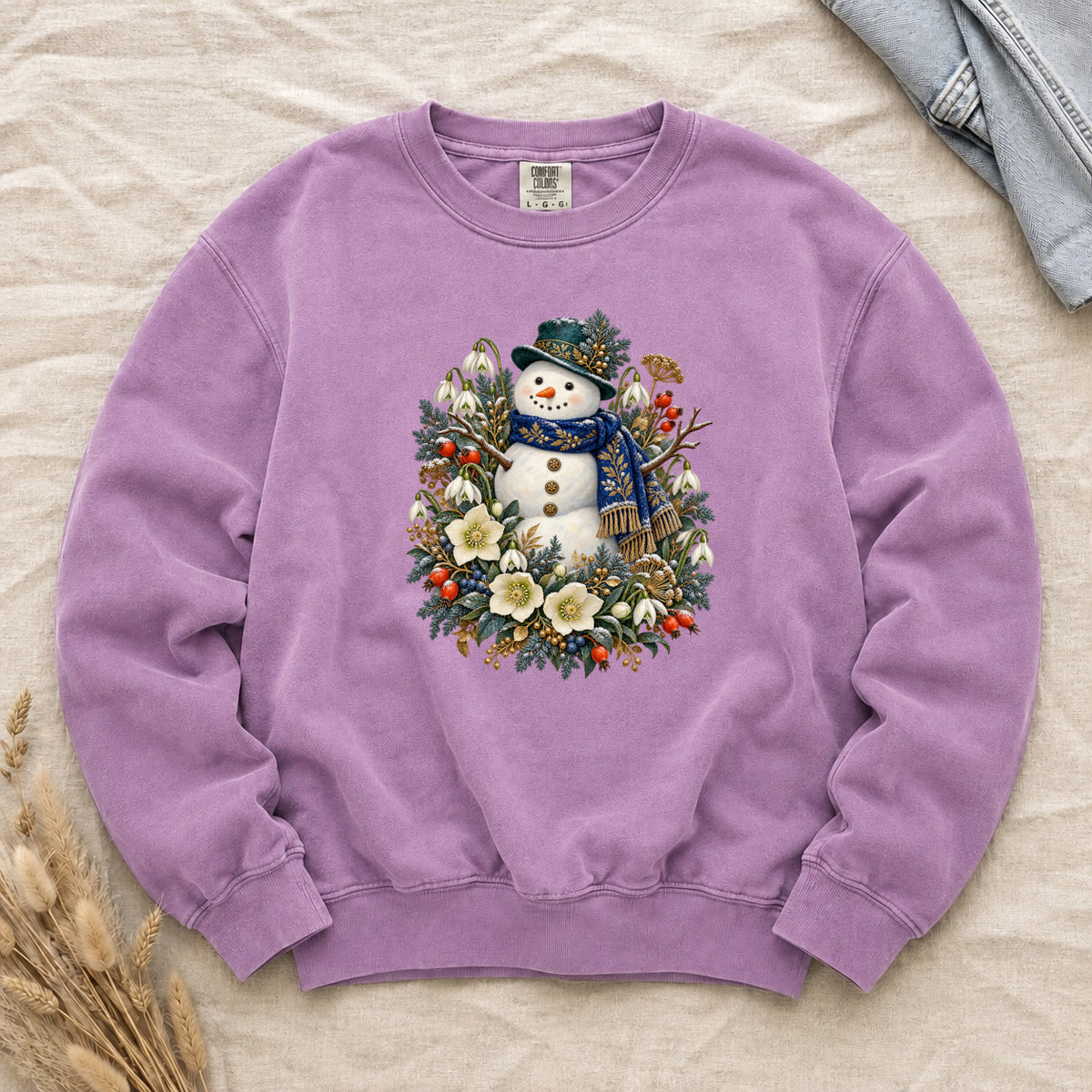 Snowman & Winter Botanicals Sweatshirt in Orchid — a smiling snowman in a decorated dark hat and a deep blue scarf with golden pattern, among evergreen branches, red berries and large cream flowers