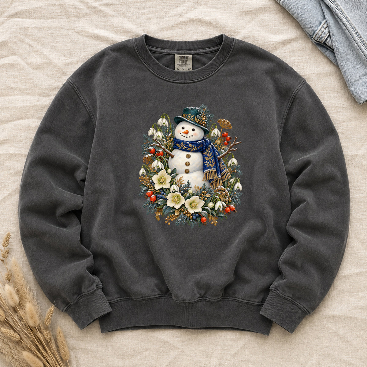 Snowman & Winter Botanicals Sweatshirt in Pepper — a smiling snowman in a decorated dark hat and a deep blue scarf with golden pattern, among evergreen branches, red berries and large cream flowers