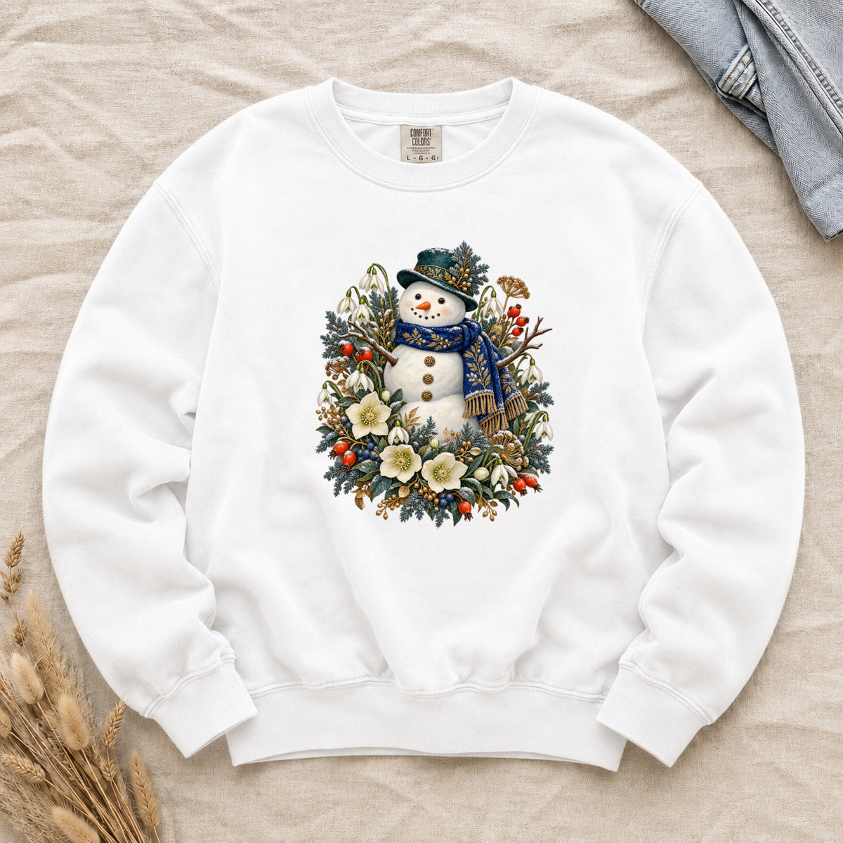 Snowman & Winter Botanicals Sweatshirt in White — a smiling snowman in a decorated dark hat and a deep blue scarf with golden pattern, among evergreen branches, red berries and large cream flowers