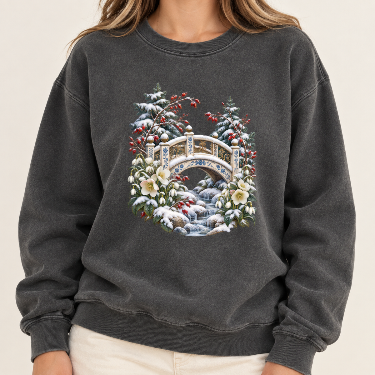 Snowy bridge and winter botanicals design on a heavyweight garment-dyed Comfort Colors 1566 crewneck — an ornate ivory footbridge arching over a snowy rocky stream, framed by evergreen, red berries and cream flowers