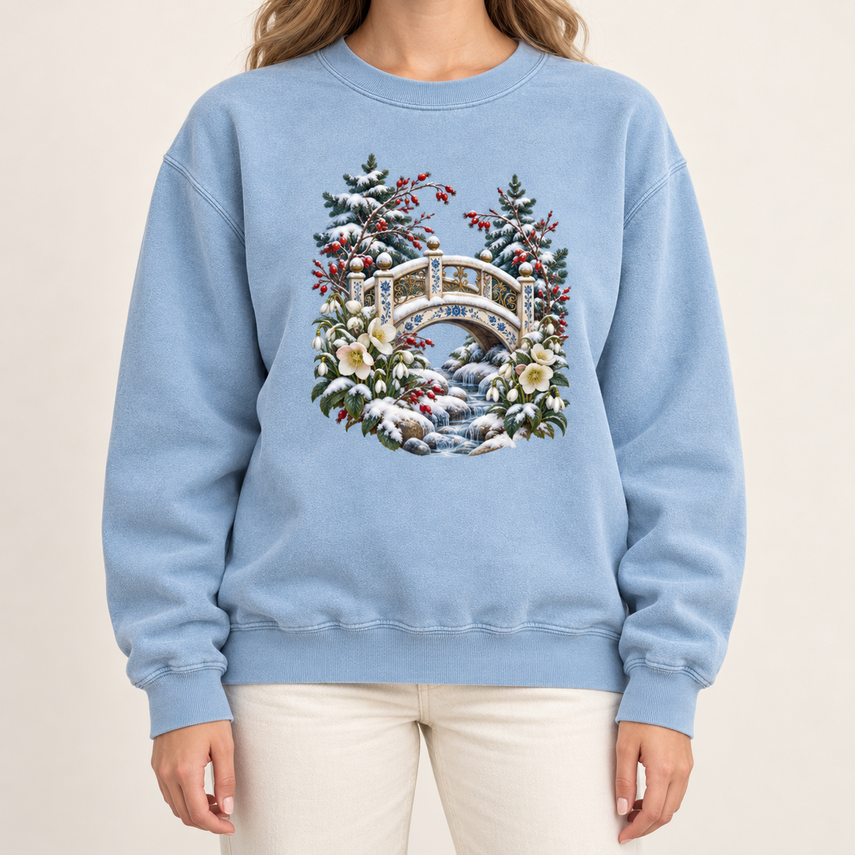 Snowy bridge and winter botanicals design on an 80/20 ring-spun cotton-blend crewneck — an ornate ivory footbridge arching over a snowy rocky stream, framed by evergreen, red berries and cream flowers
