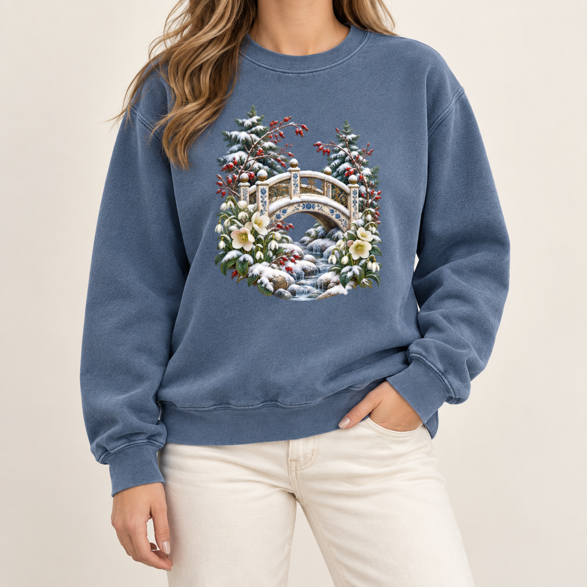 Snowy bridge winter landscape sweatshirt, relaxed unisex fit, adult sizes S to 3XL — an ornate ivory footbridge arching over a snowy rocky stream, framed by evergreen, red berries and cream flowers