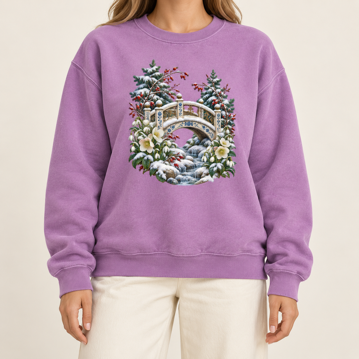 Snowy bridge winter crewneck with 1x1 ribbed collar, cuffs and waistband — an ornate ivory footbridge arching over a snowy rocky stream, framed by evergreen, red berries and cream flowers