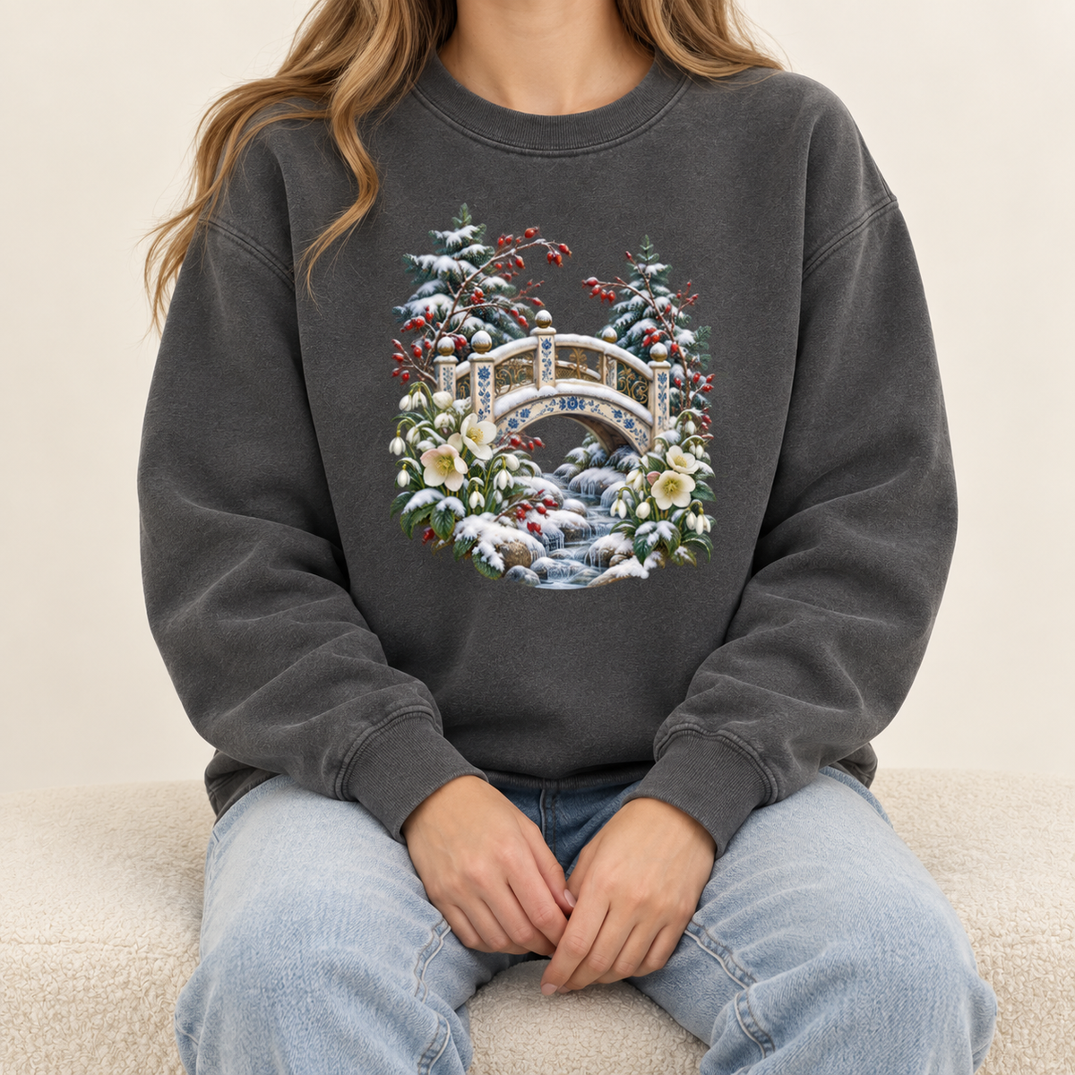 Snowy bridge and winter botanicals sweatshirt, large front-centered print, no lettering — an ornate ivory footbridge arching over a snowy rocky stream, framed by evergreen, red berries and cream flowers
