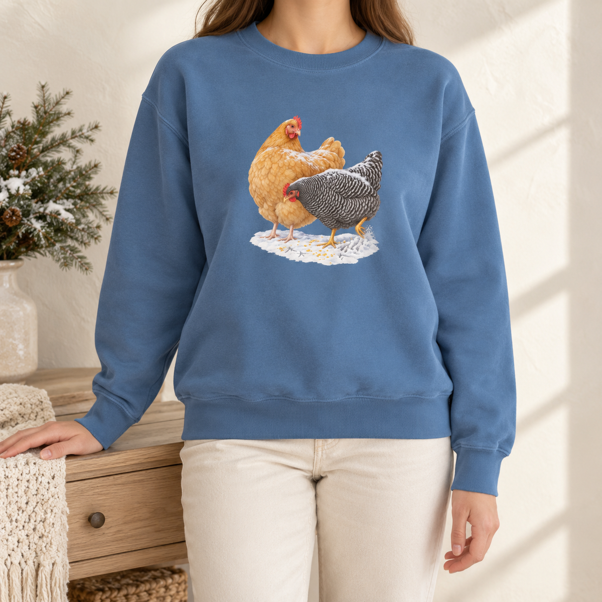 Winter hens sweatshirt in Blue Jean worn by a woman – a watercolor Buff Orpington and Barred Rock hen in the snow with corn and tracks, printed large on a garment-dyed Comfort Colors crewneck