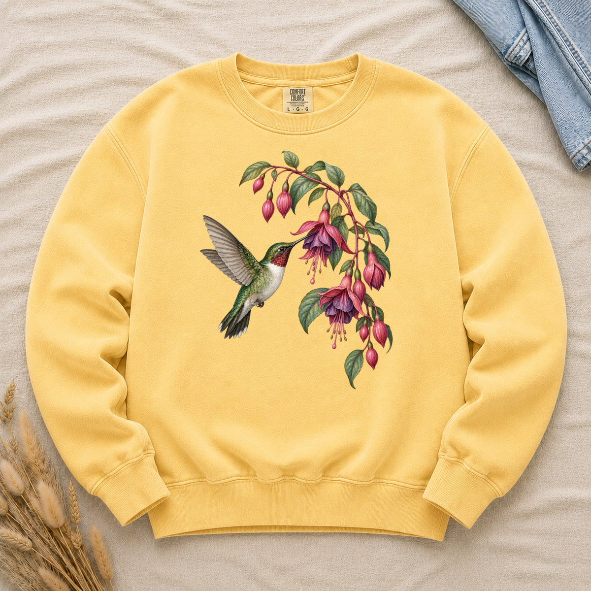 Stay a Little Longer sweatshirt in Butter, a hummingbird hovering beneath cascading pink and purple fuchsia blossoms