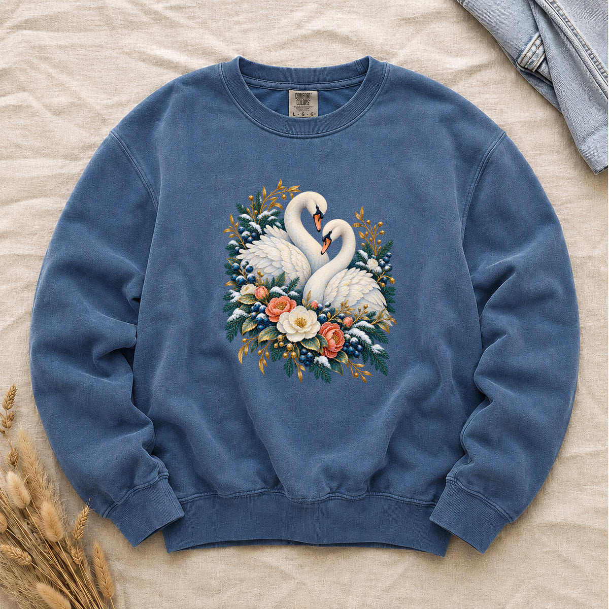 Swan Pair & Floral Sweatshirt in Blue Jean — two ivory swans turned toward one another with their necks curving together, among deep green foliage, blue berries and golden sprigs, cream and coral flowers gathered beneath