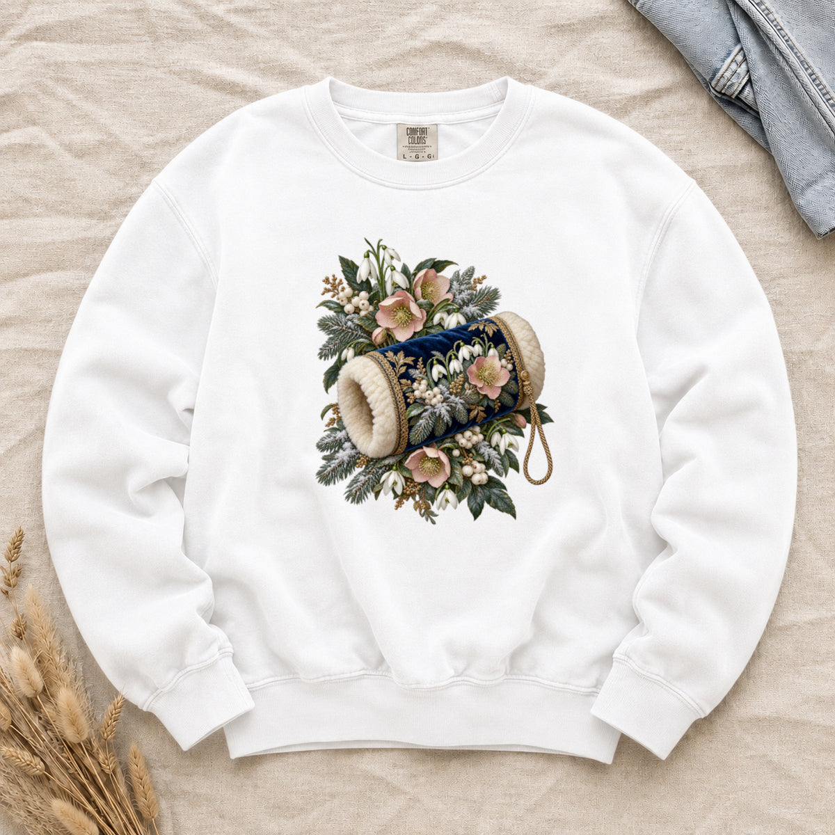 Vintage Hand Muff and Winter Florals Sweatshirt in White — an ornate navy hand muff with fluffy cream trim and gold botanical detail, resting among evergreen branches, white snowdrops, soft pink flowers and pale berries