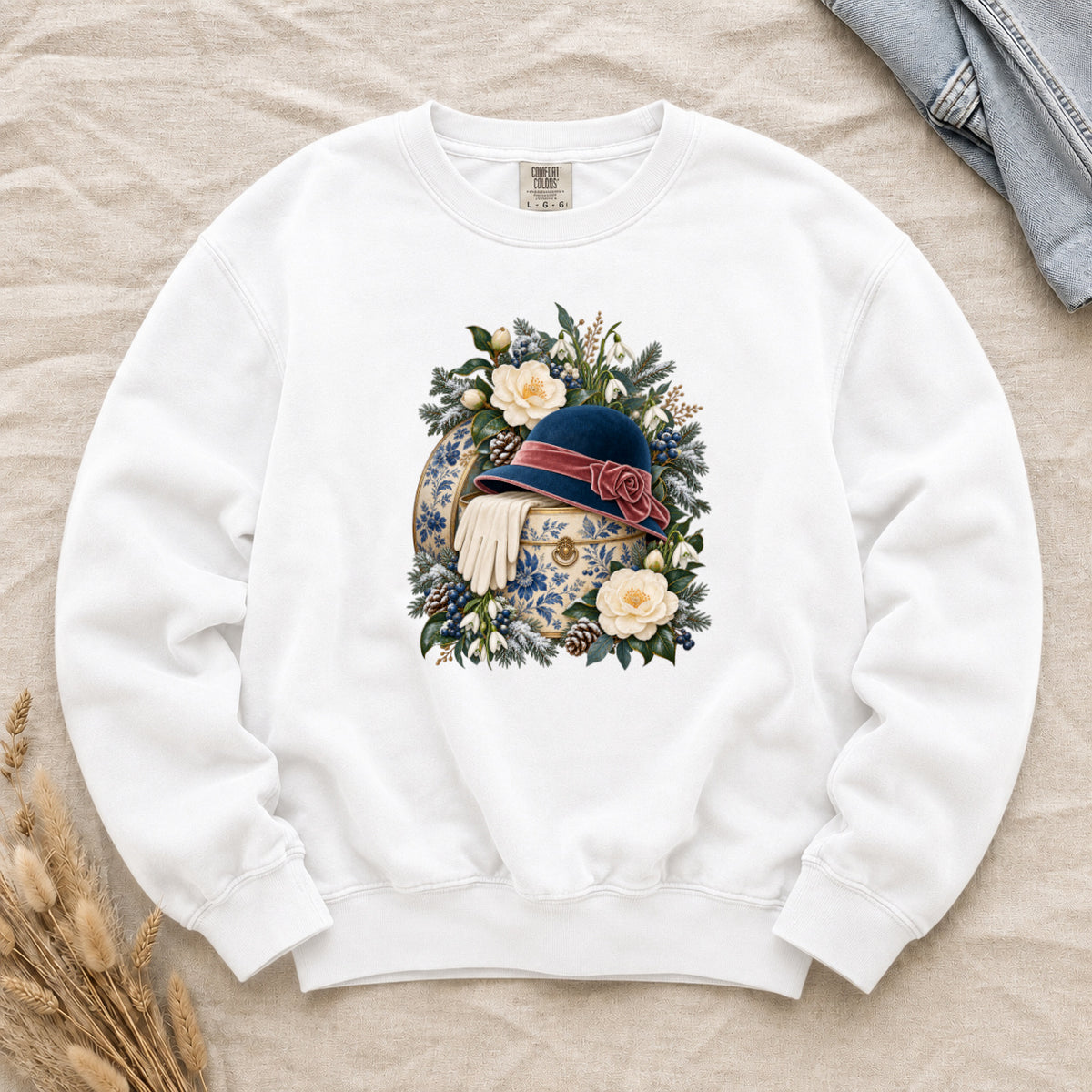 Vintage Cloche Hat and Winter Florals Sweatshirt in White — a navy cloche hat with a dusty rose ribbon and rosette on a cream hatbox patterned in blue florals, ivory gloves over the edge among snowdrops, blue berries and snow-dusted evergreen