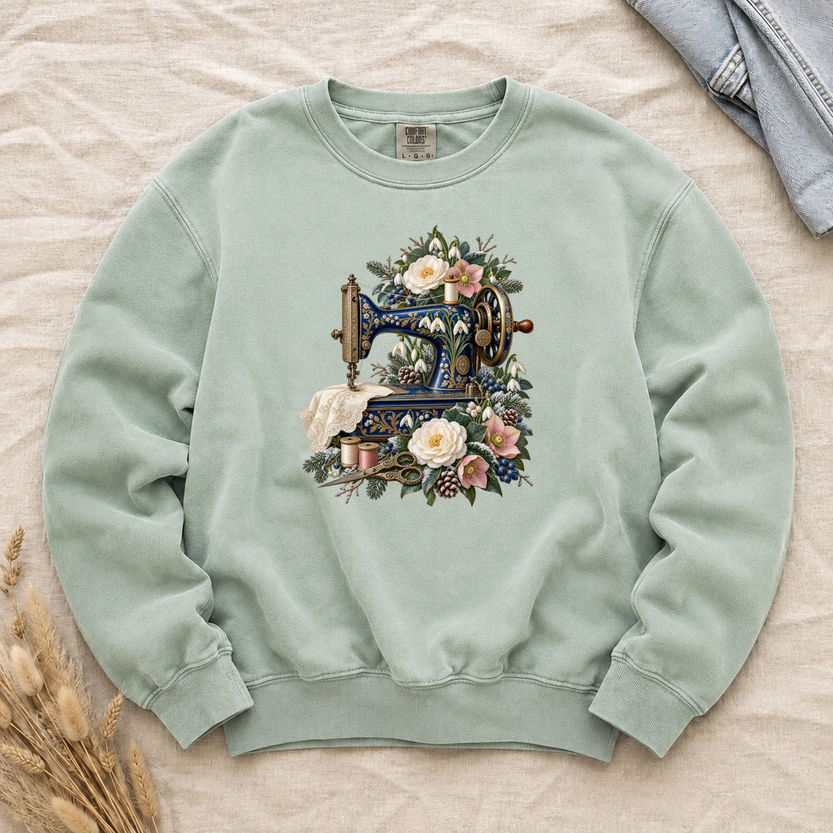 Vintage Sewing Machine and Winter Florals Sweatshirt in Chalky Mint — an ornate blue sewing machine with gold detailing among cream and muted pink flowers, evergreen sprigs, berries and pinecones, with lace draped from the sewing bed